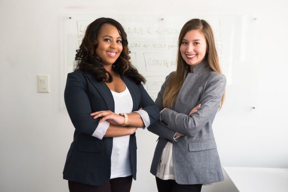 Business People - two women in suits standing beside wall