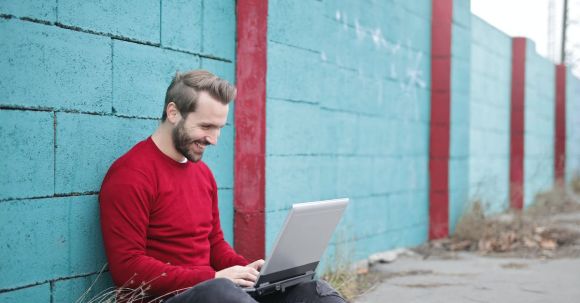 Online Business - Man Leaning Against Wall Using Laptop
